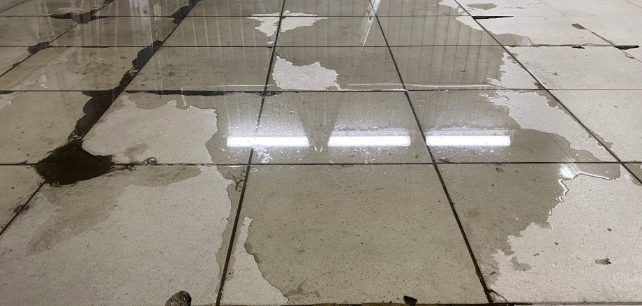 Auf einem Fließenboden ist eine Wasserpfütze.