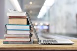 Laptop und Bücherstapel Ein geöffneter Laptop steht neben einem Bücherstapel auf einem Holztisch.