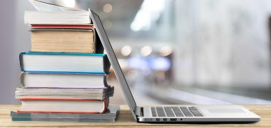 Ein geöffneter Laptop steht neben einem Bücherstapel auf einem Holztisch.