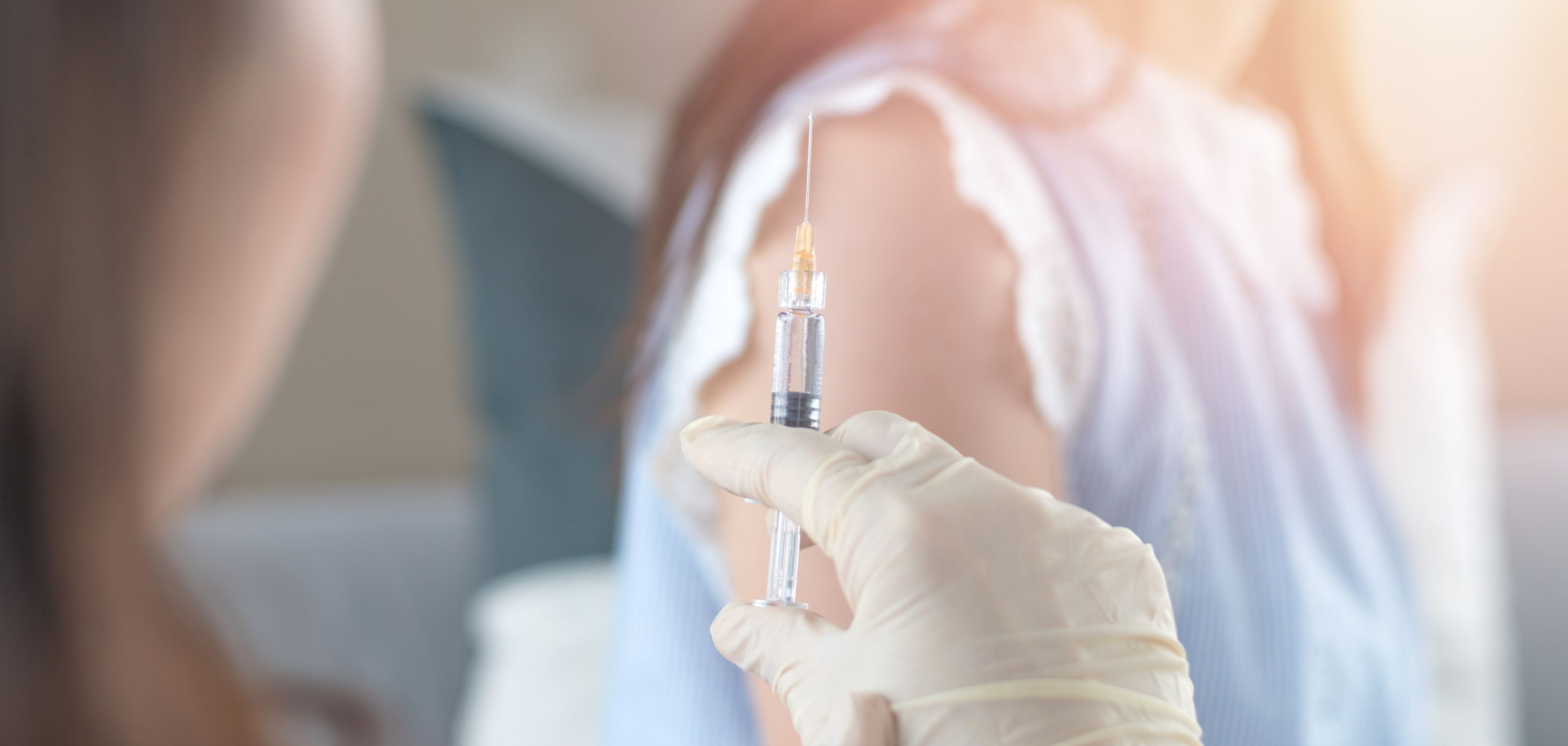 Eine Frau wartet auf ihre HPV-Impfung, die eine Ärztin in der Hand hält.