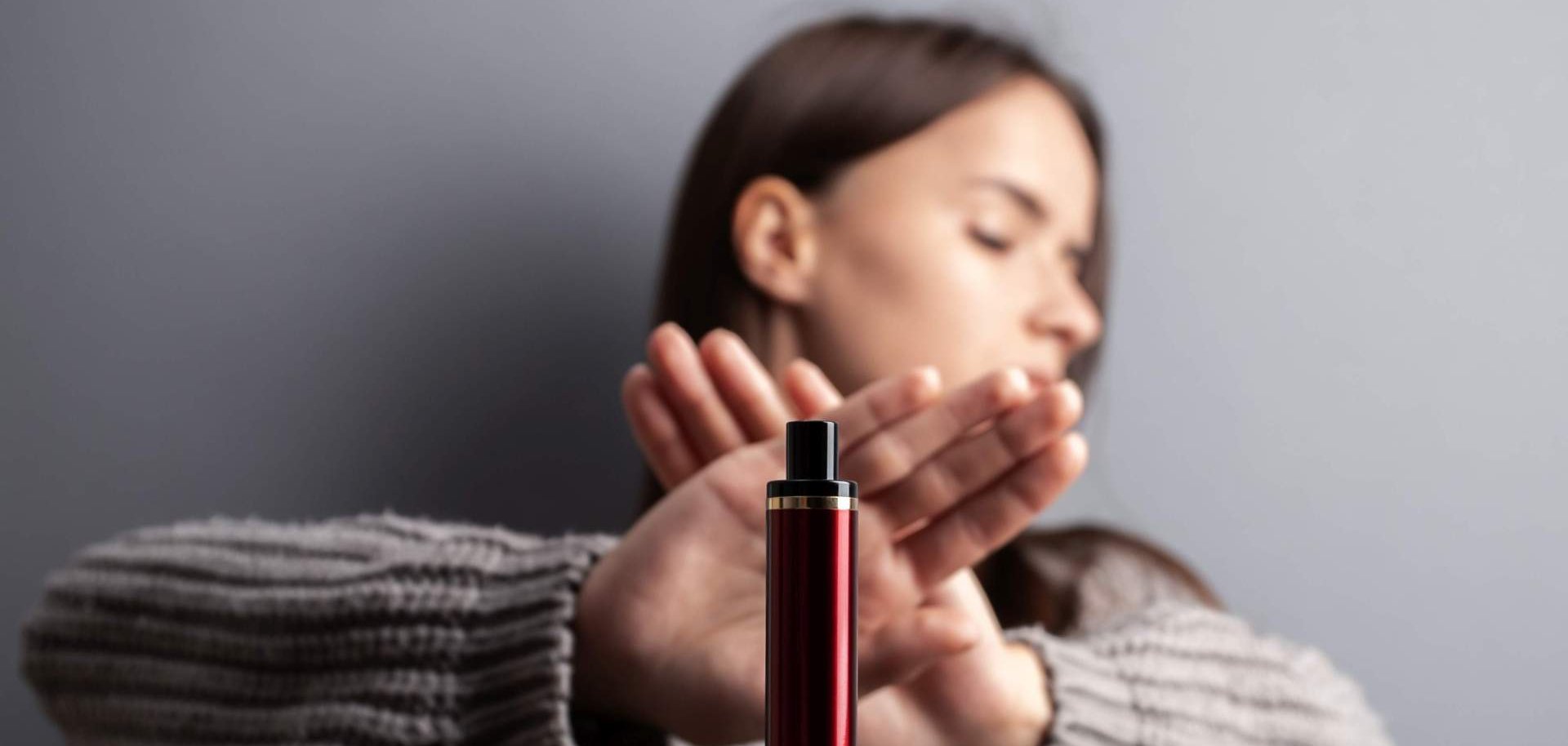 Einem jungen Mädchen wird eine Vape vor das Gesicht gehalten. Sie verschränkt die Hände vor dem Gesicht in einer abwehrenden Geste.