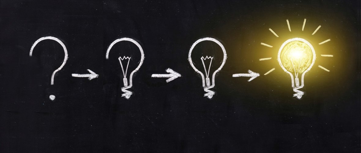 Eine Tafel, auf der drei Glühbirnen mit weißer Kreide gemalt sind. Ganz rechts leuchtet eine echte Glühbirne.