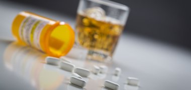 Several Prescription Drugs Spilled From Fallen Bottle Near Glass of Alcohol.