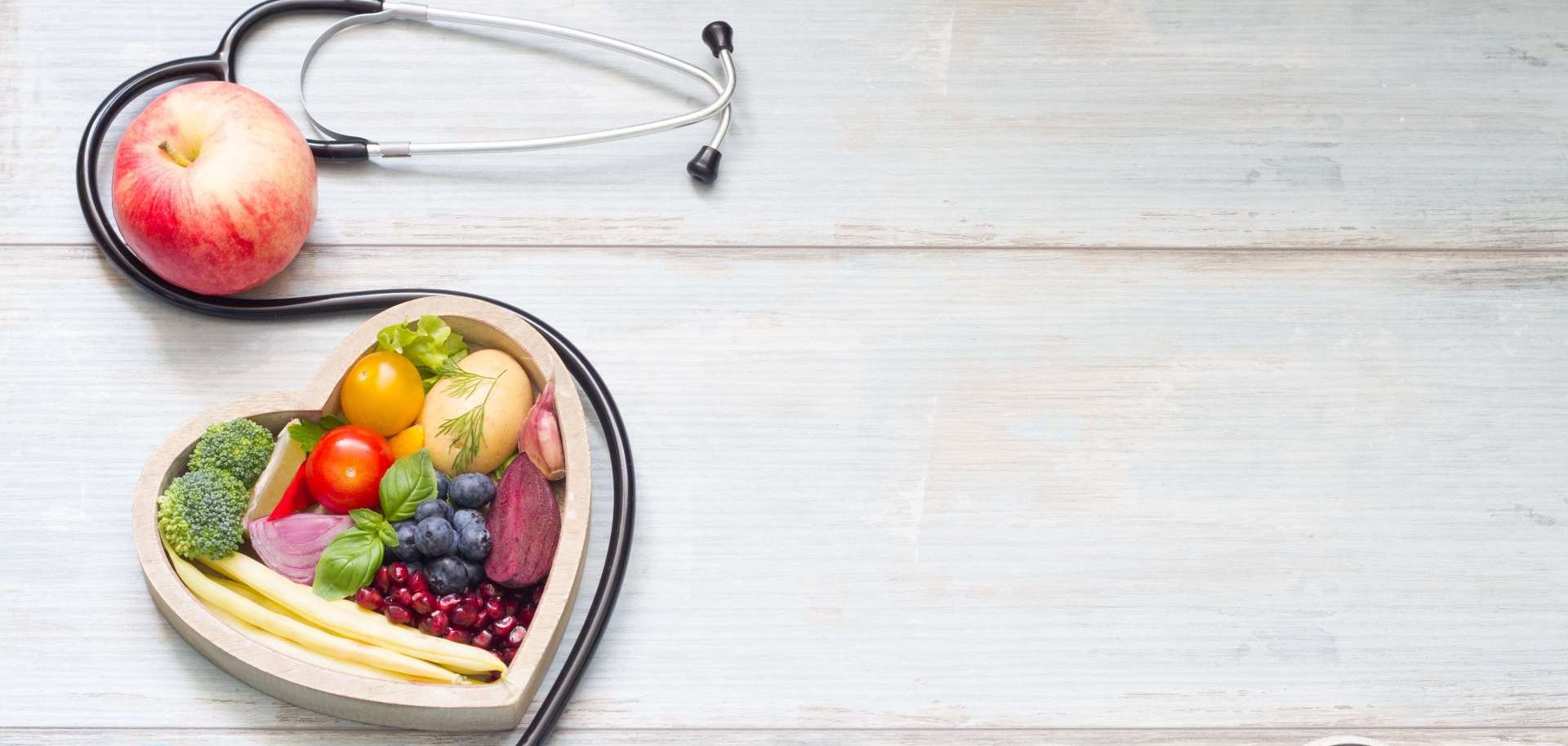 Das Symbolfoto für Gesundheit zeigt ein Stethoskop, ein Herz aus Gemüse und kleinere Trainingsgeräte wie zum Beispiel Hanteln.