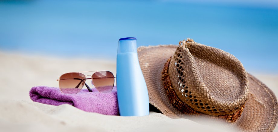 Am Strand liegen Sonnenschutzcreme und ein Strohhut 