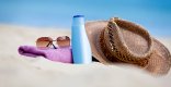 Am Strand liegen Sonnenschutzcreme und ein Strohhut 
