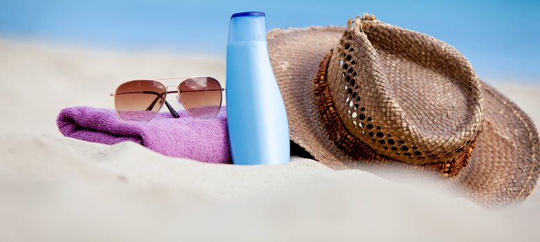 Sonnenschutz Am Strand liegen Sonnenschutzcreme und ein Strohhut
