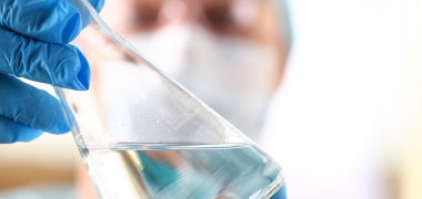 Ein Labormitarbeiter hält ein Reagenzglas mit einer klaren Flüssigkeit hoch