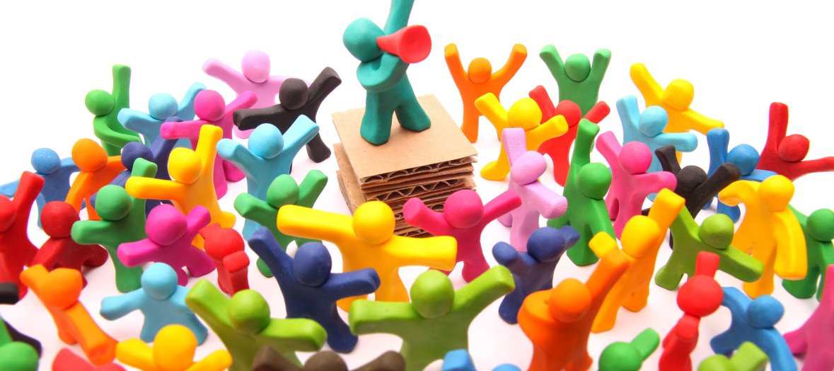 Männchen mit Megaphon auf Podest inmitten von bunten Zuhörern Figur mit Megaphon auf Podest inmitten von bunten Figurzuhörenden