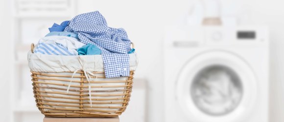 Ein hölzerner Wäschekorb gefüllt mit blauen und weißen Kleidungsstücken steht vor einer weißen Waschmaschine.