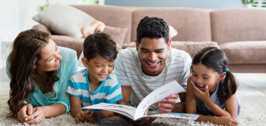 Eltern und zwei Kinder liegen auf dem Boden und schauen in ein Buch 