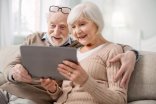 Älteres Pärchen schauen in ein Tablet auf der Couch