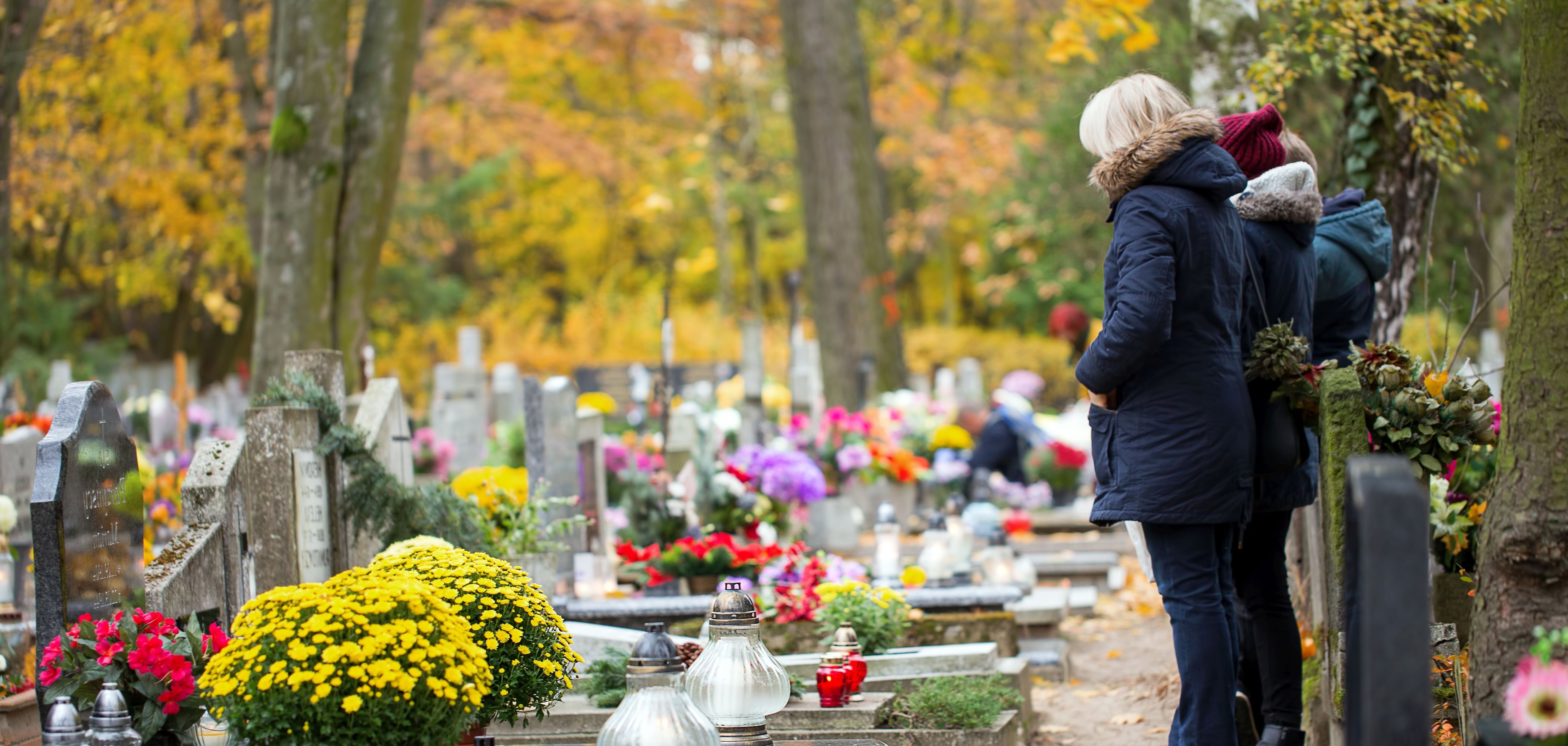Menschen beten an einem Grab auf einem herbstlichen Friedhof.