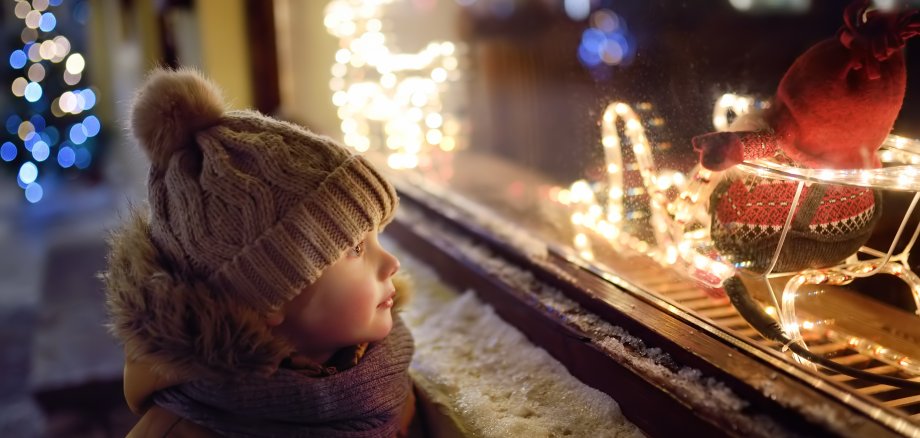 Kleines Kind schaut in Schaufenster nach leuchtendem Weihnachtsmann