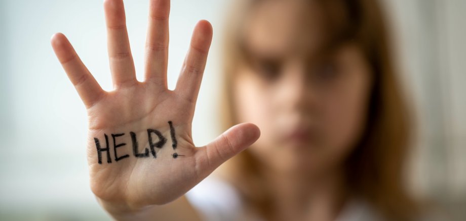 Ein kleines Mädchen hält ihre Hand hoch. Auf deren Innenseite steht das Wort "help" geschrieben.