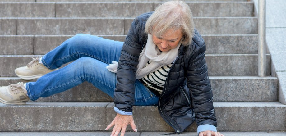 Das Bild zeigt eine ältere Frau, die im Außenbereich eine Treppe hinuntergestürzt ist.