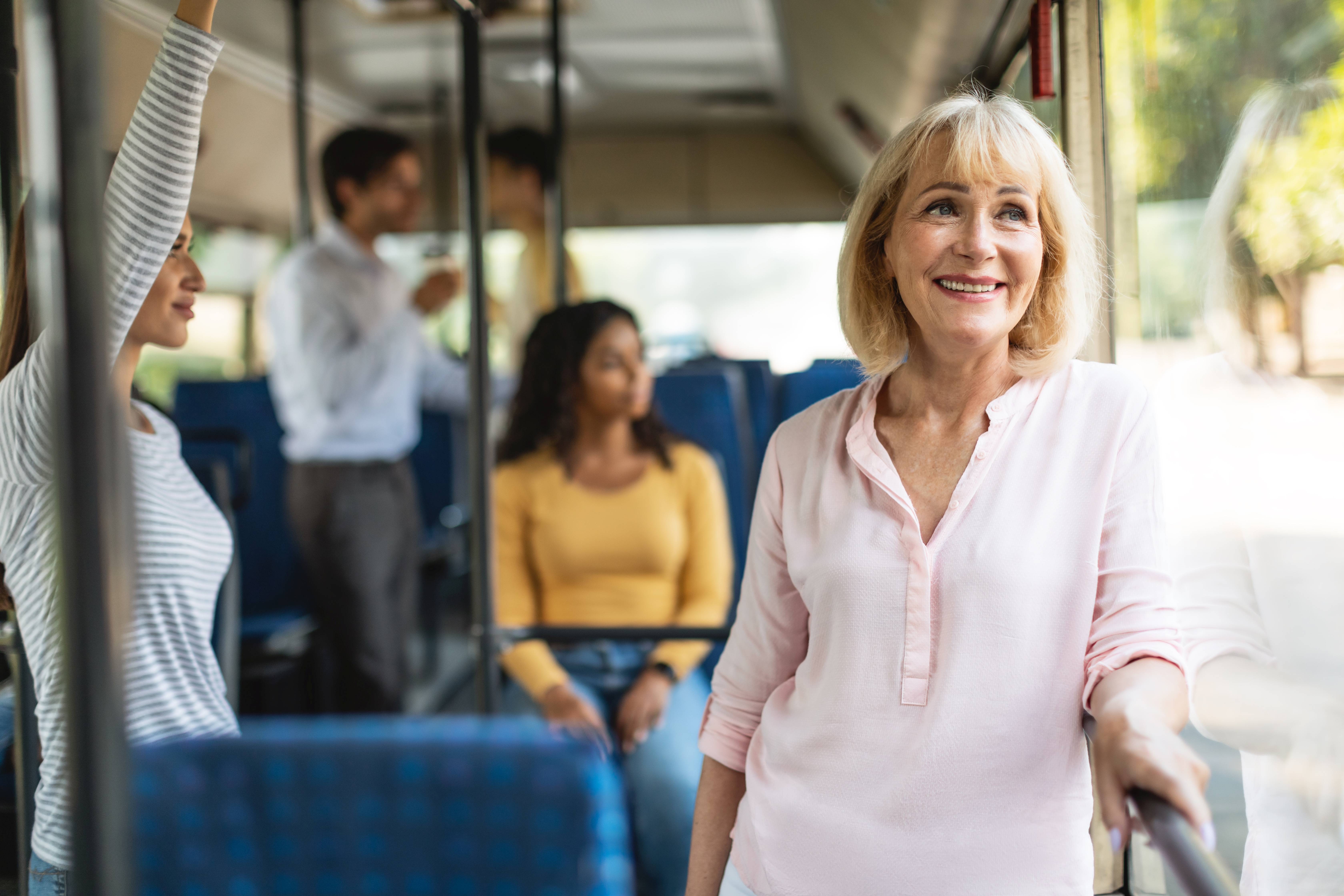 Eine ältere Frau fährt stehend in einem Bus.