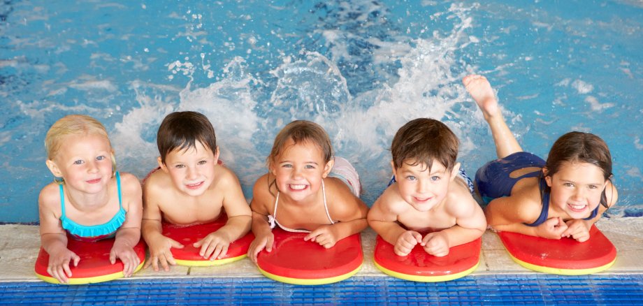 Das Bild zeigt eine Gruppe von Kindern am Beckenrand in einem Schwimmbad