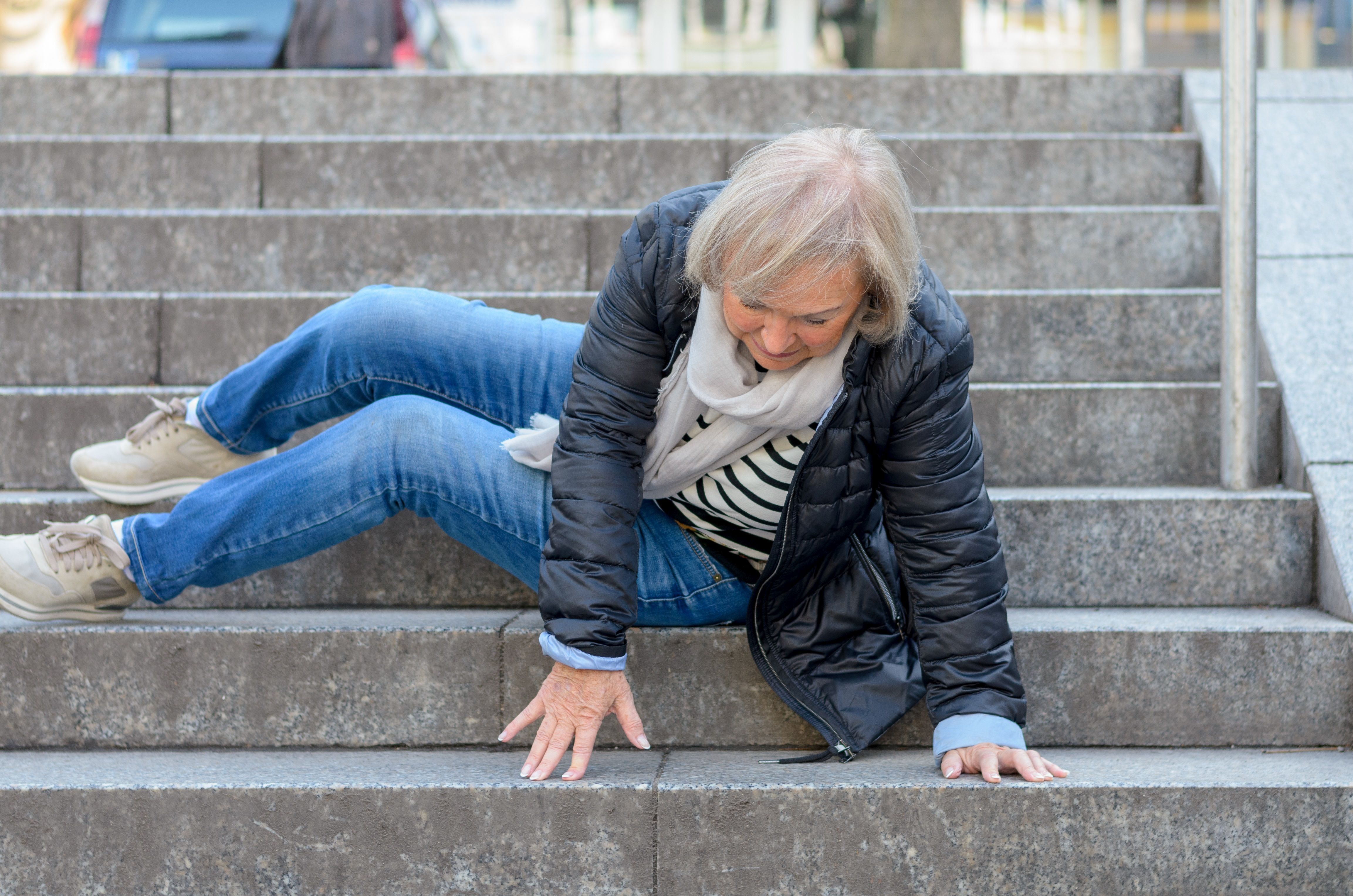 Das Bild zeigt eine ältere Frau, die im Außenbereich eine Treppe hinuntergestürzt ist.
