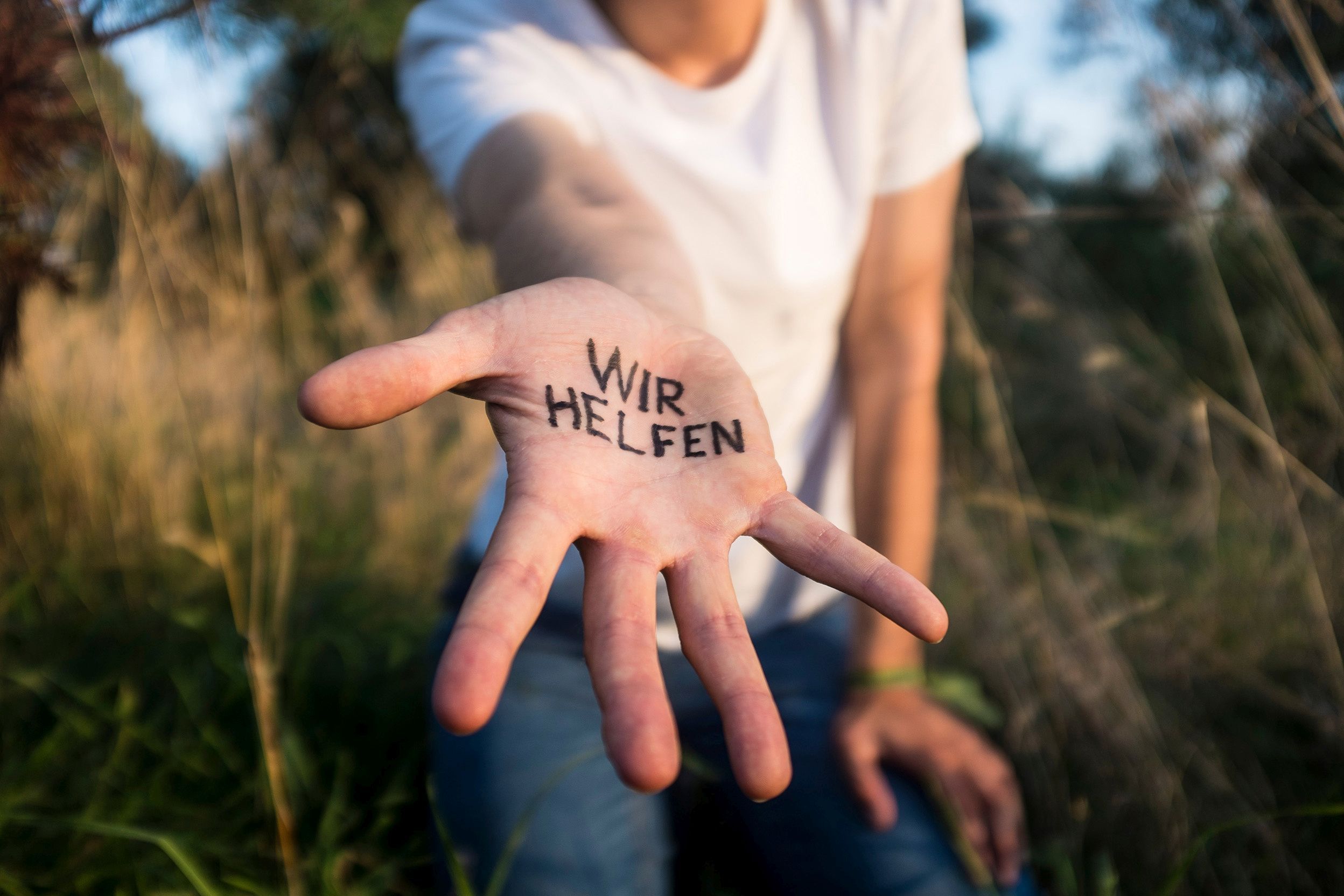 Hand streckt sich zur Kamera aus und hat Schriftzug "wir helfen" drauf