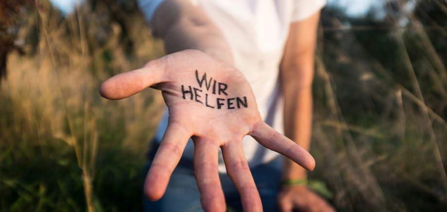 Helfende Hand Hand streckt sich zur Kamera aus und hat Schriftzug "wir helfen" drauf