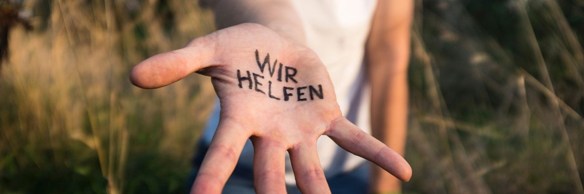 Helfende Hand Hand streckt sich zur Kamera aus und hat Schriftzug "wir helfen" drauf