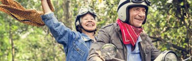 Seniorin und Senior fahren in der Natur auf einem Roller