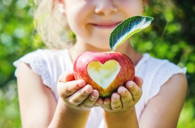 Mädchen hält einen Apfel. Ein Herz ist in den Apfel geschnitzt.