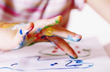 Nahaufnahme von einer Kinderhand, die mit Fingerfarben etwas auf ein weißes Blatt Papier malt.