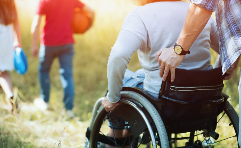 Frau im Rollstuhl wird von einem Mann auf einer Wiese geschoben