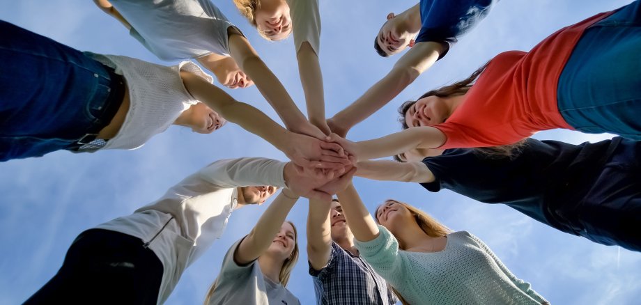 Eine Gruppe von junger Menschen legt sternförmig die Hände übereinander.
