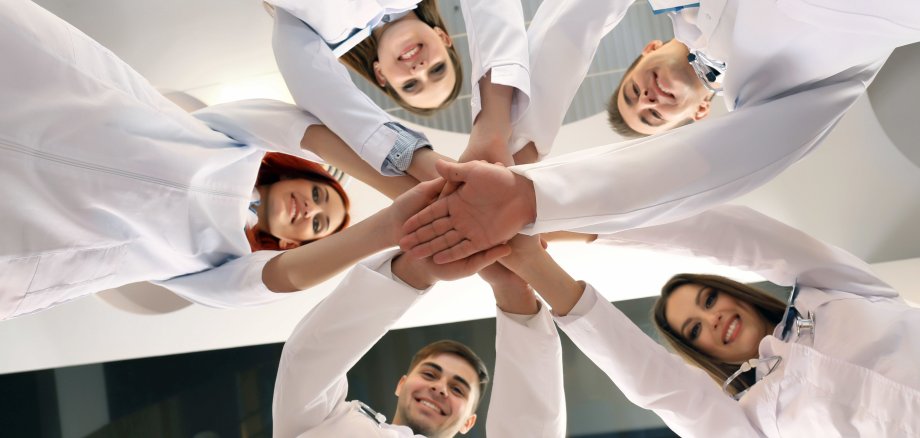 United hands of medical team close up 5 Ärzte halten jeweils eine Hand über die anderen in die Mitte