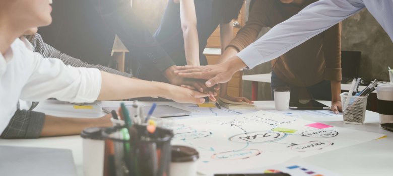 Ein Arbeitsteam legt Hände über einem Schreibtisch zusammen