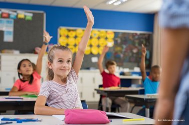 Schülerin meldet sich in der Schule und schaut den Lehrer konzentriert an