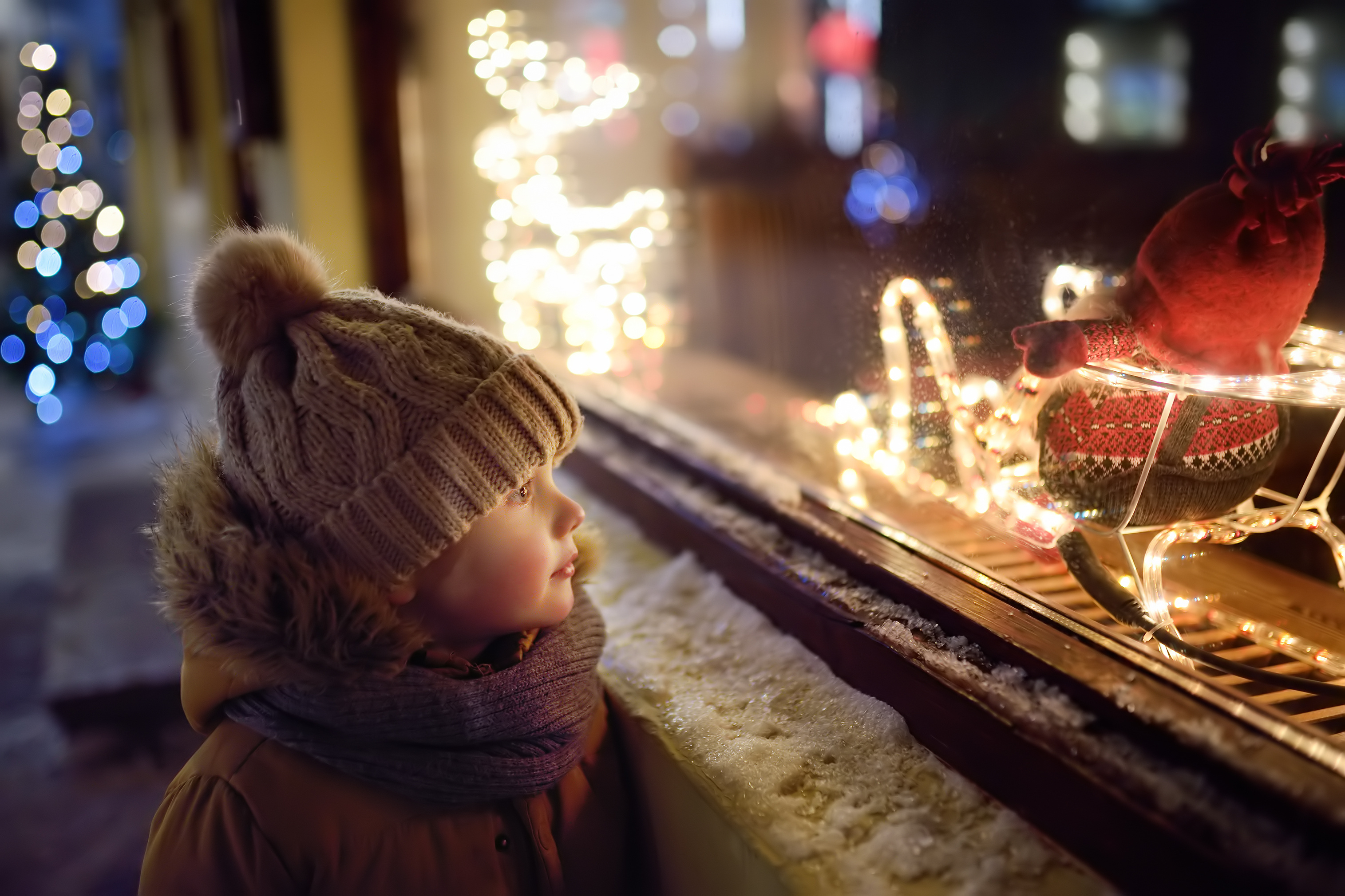 Kleines Kind schaut in Schaufenster nach leuchtendem Weihnachtsmann