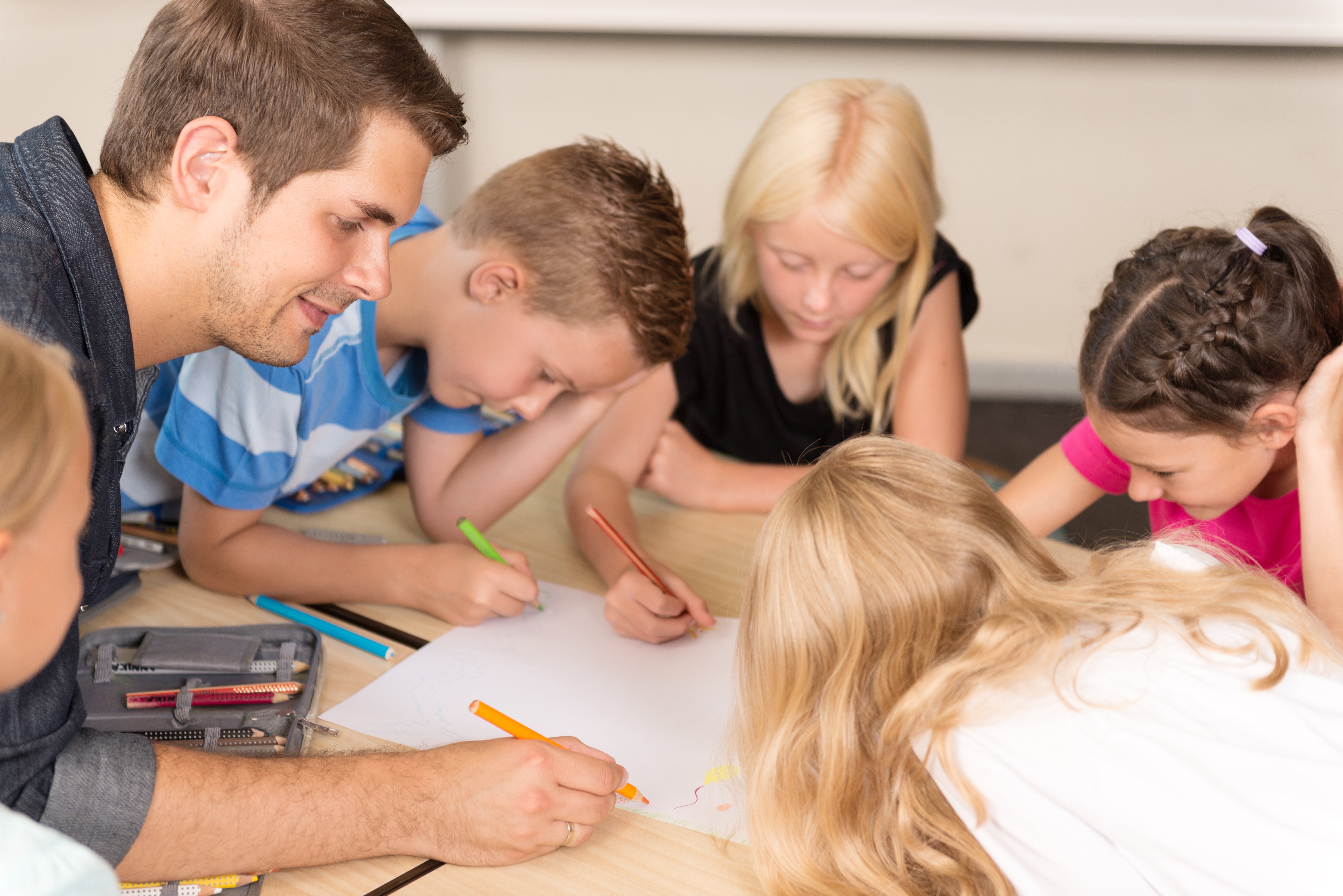 Das Bild zeigt einen Betreuer, der mit mehreren Grundschulkindern bei der Nachmittagsbetreuung am Tisch sitzt und mit ihnen malt.
