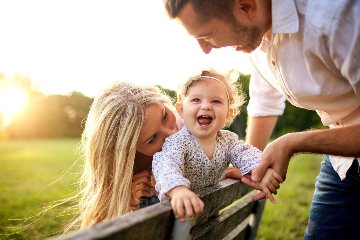 Familie mit Baby im Park Vater und Mutter mit lachendem Baby auf Parkbank