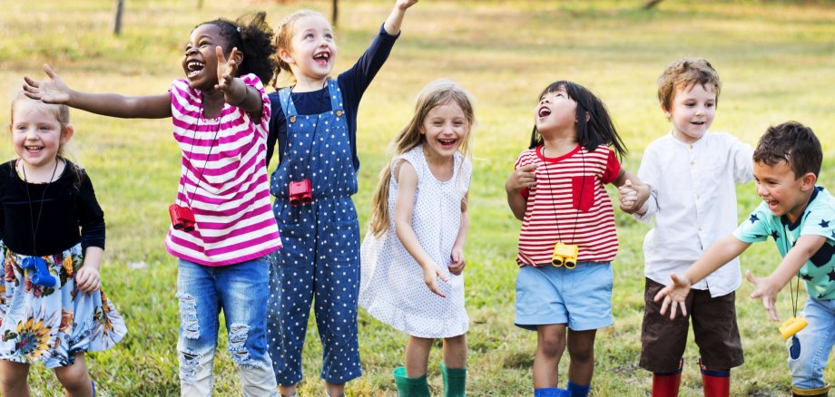 Eine Gruppe Kinder verschiedener Nationalitäten spielen begeistert auf einer Wiese