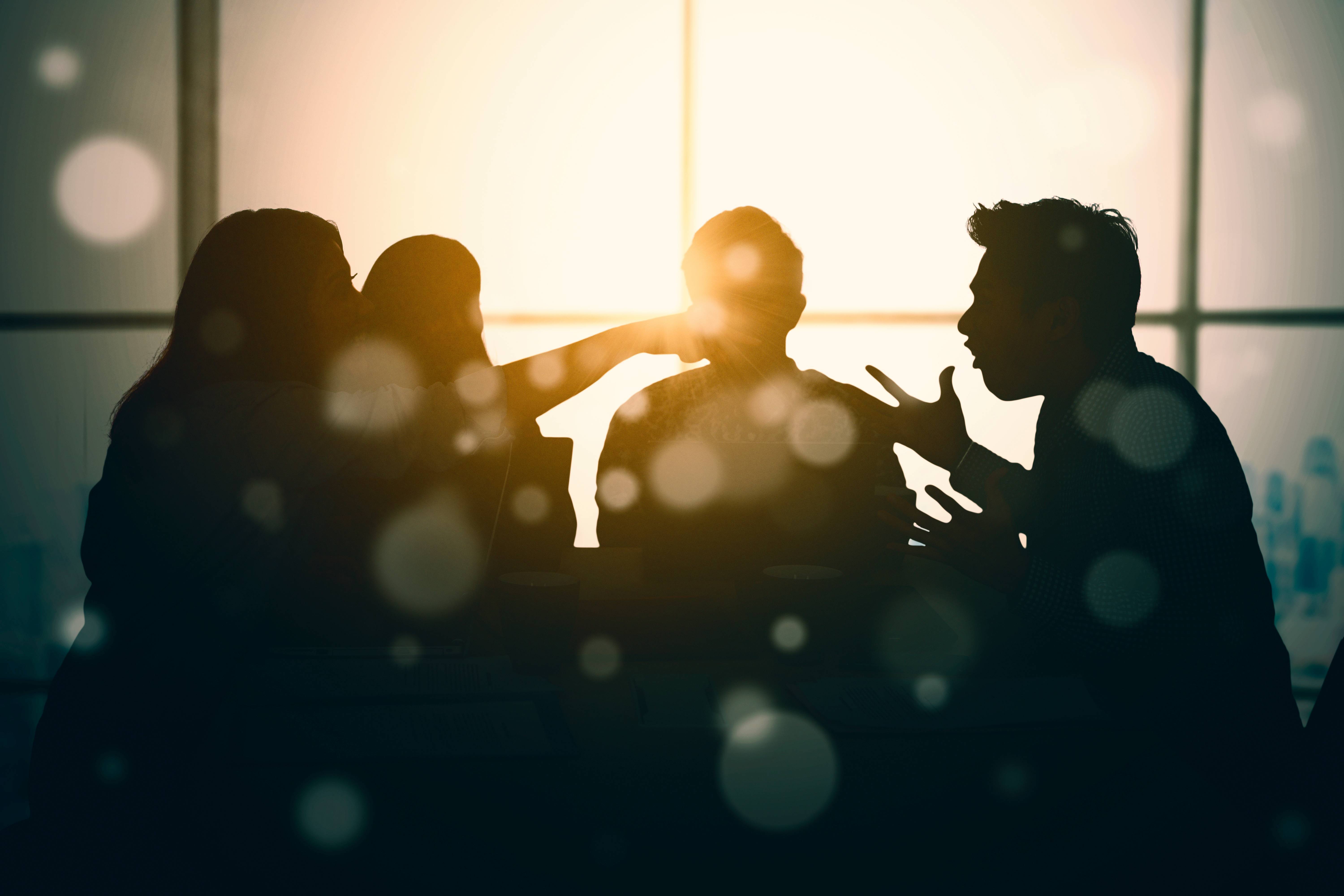 In einer Silhouette sind im Sonnenlicht mehrere Menschen zu sehen, die miteinander streiten.