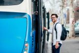 Mann am Bus Ein junger dunkelhaariger Mann mit Brille steigt lächelnd in einen blauen Bus.