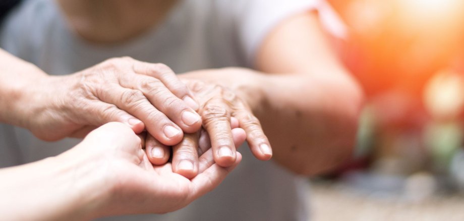 Ein paar Hände halten die Hand einer Seniorin.