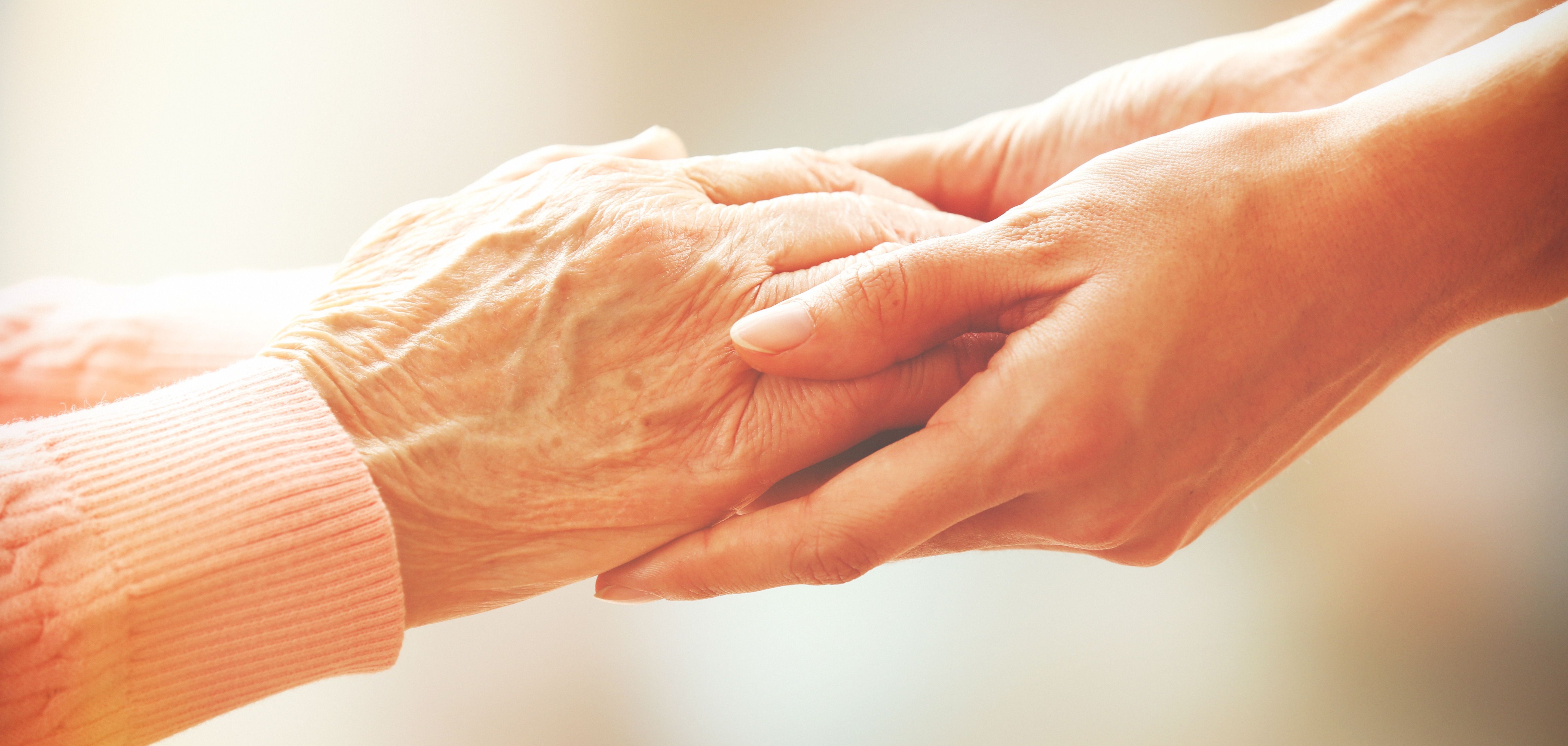 Ein paar Hände halten die Hände einer älteren Person.