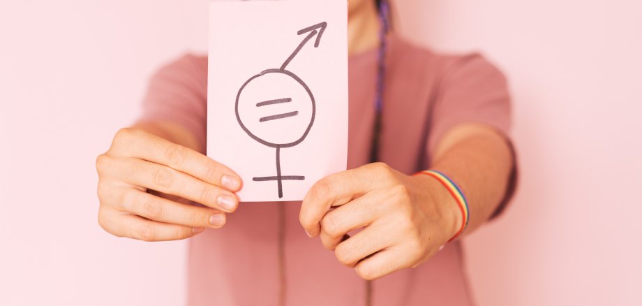 Girl holding paper with gender equality sign against pink background Girl holding paper with gender equality sign against pink background