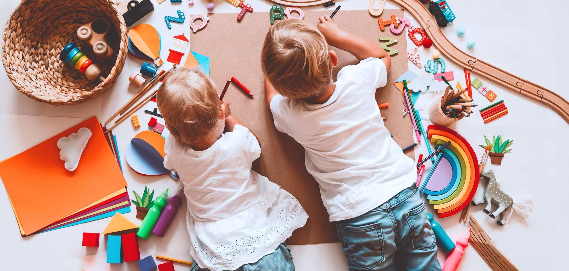 Zwei Kinder liegen zwischen Spielsachen auf dem Boden und maleb.