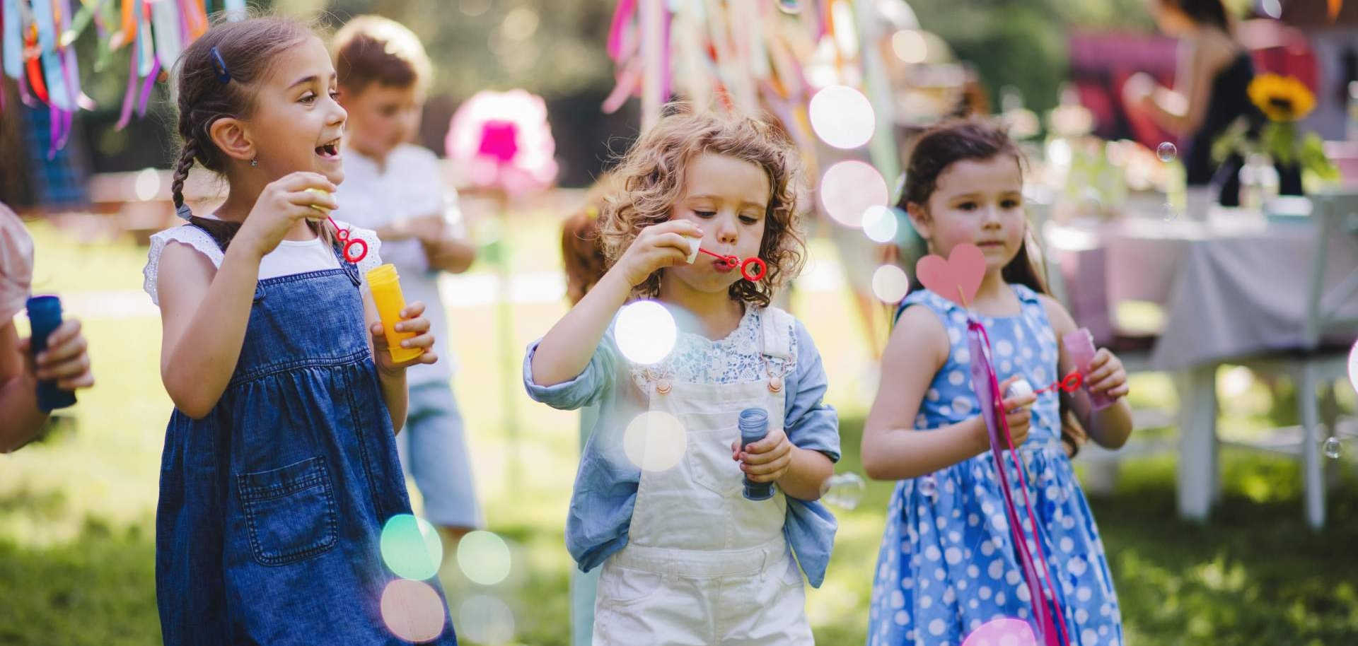Zwei kleine Mädchen spielen in einem Garten mit Seifenblasen.
