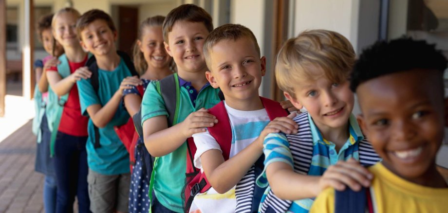 Eine Gruppe Schulkinder stehen hintereinander in einer Reihe mit den Händen auf den Schultern der jeweiligen Vorderperson.