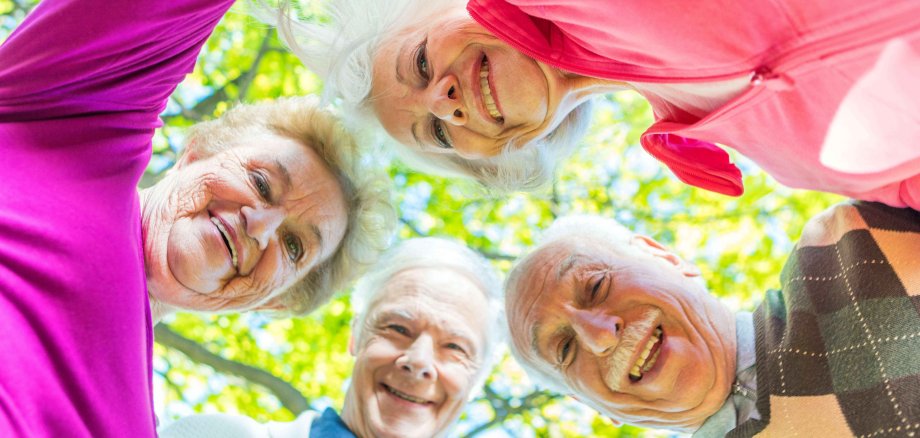 Vier Senioren und Seniorinnen stehen draußen in einem Kreis und lachen in die Kamera.