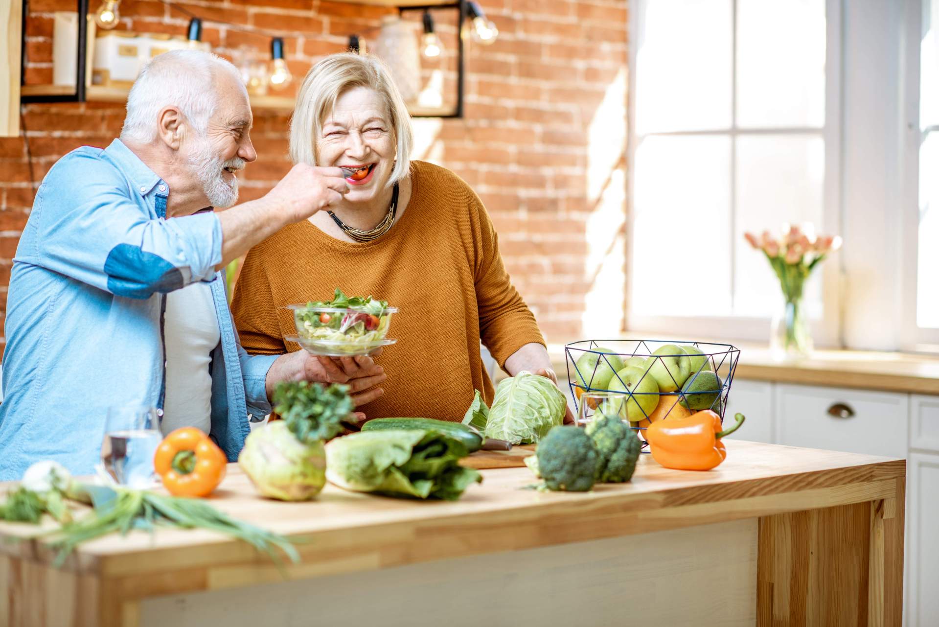 Ernährung bei Demenz Ein glückliches Seniorenpaar bereitet gemeinsam lachend Essen zu.