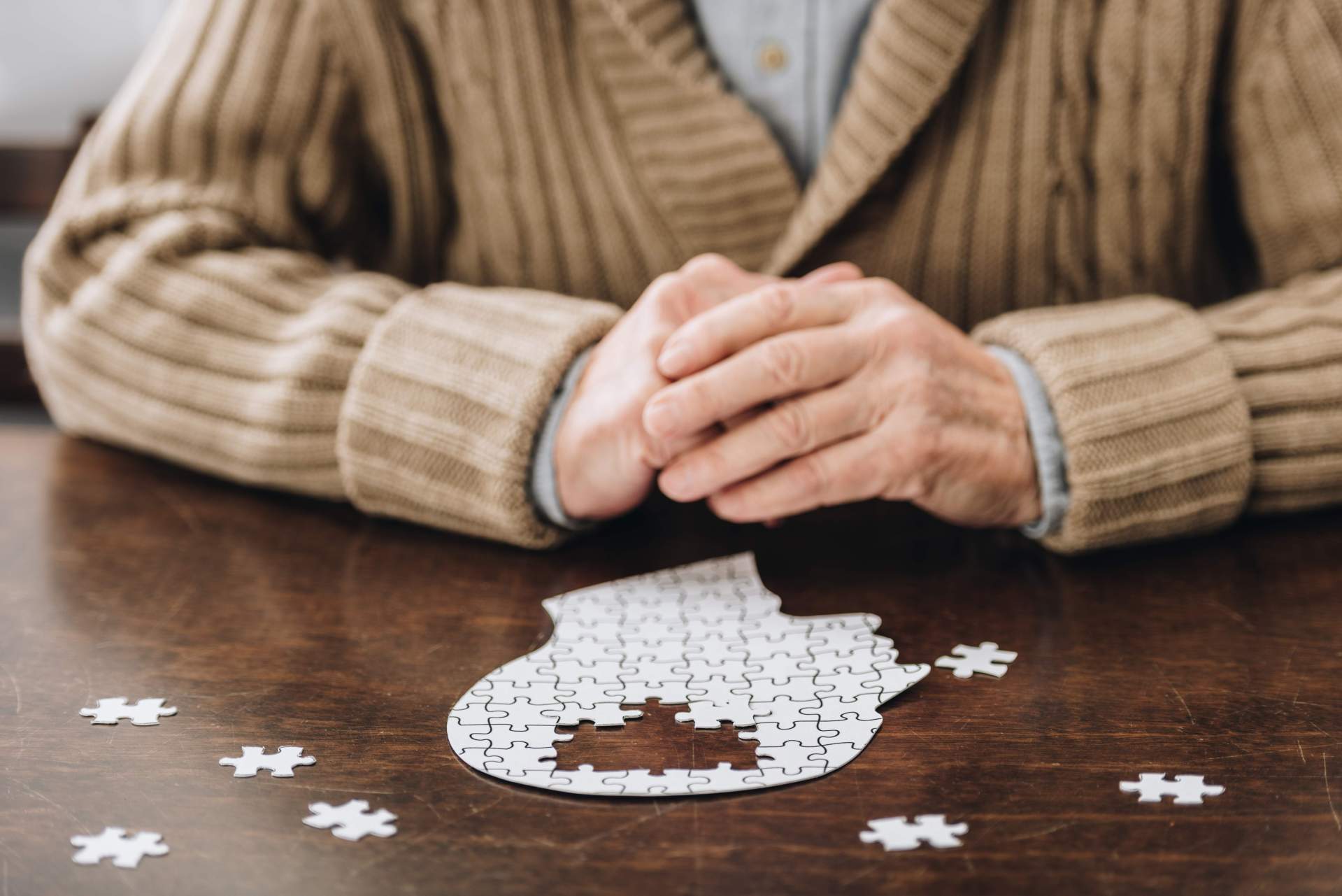 Welt-Alzheimertag Ein Senior sitzt an einem Tisch vor einem Puzzle, in der Form eines Kopfes.
