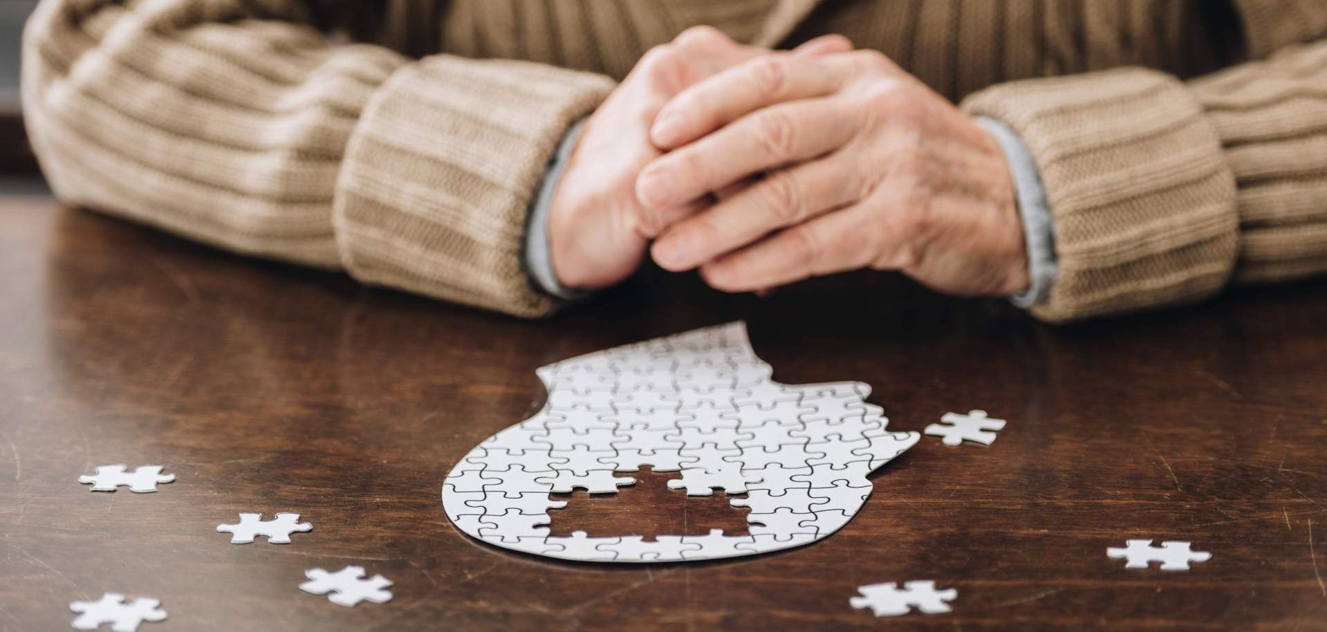 Ein Senior sitzt an einem Tisch vor einem Puzzle, in der Form eines Kopfes.